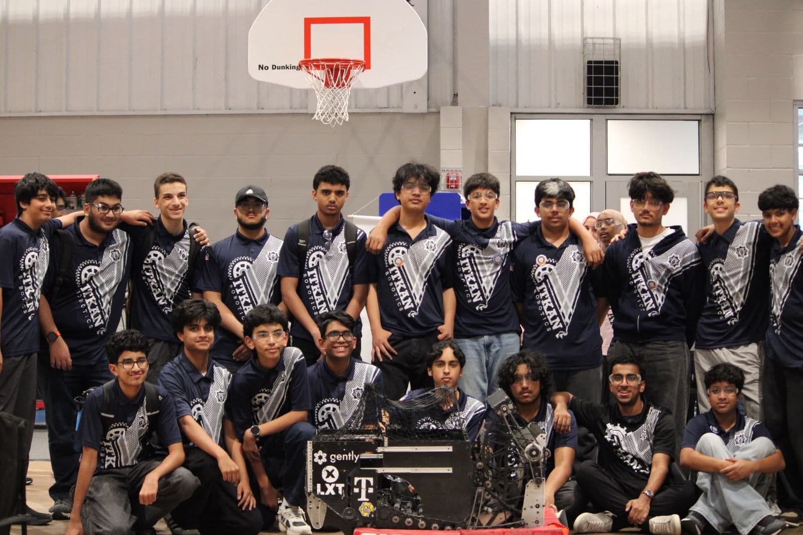ITKAN Robotics Team 9128 members in navy ITKAN polos, posed with their robot in the gym at NTX