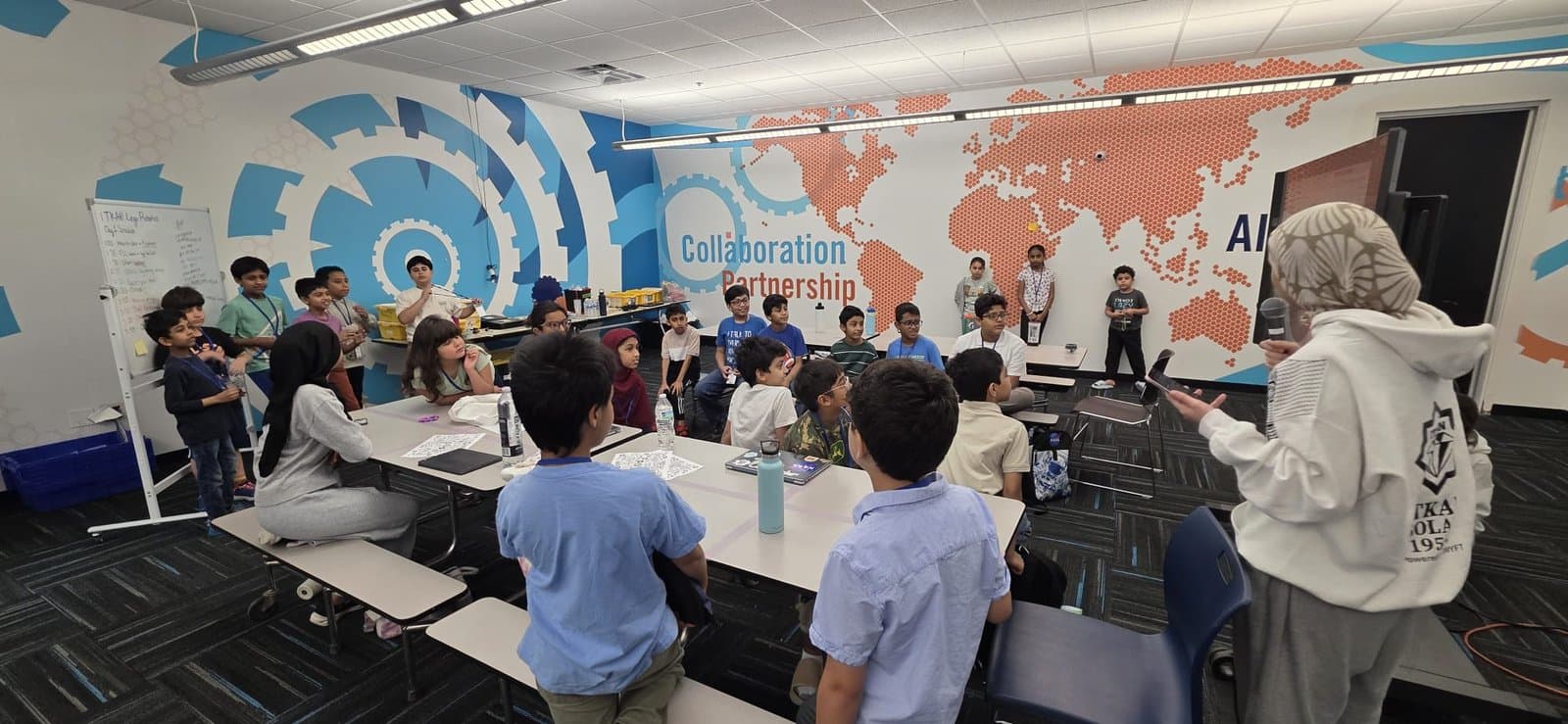 Coaches address students seated at tables in the Innovation Hub's Collaboration and Partnership room