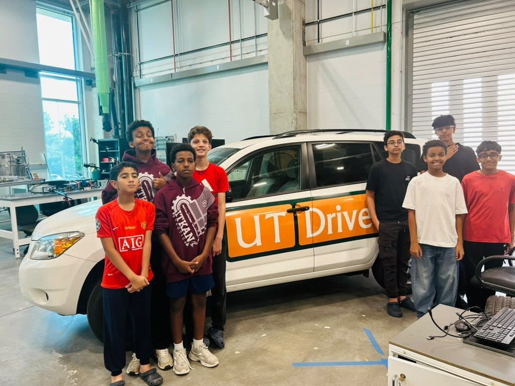 Team members beside a white SUV with an orange UT Drive logo