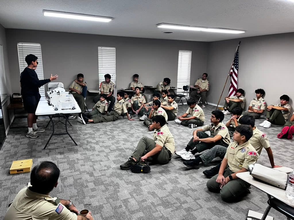 Boy Scouts sit on the floor as a team member presents the robot at the front of the room