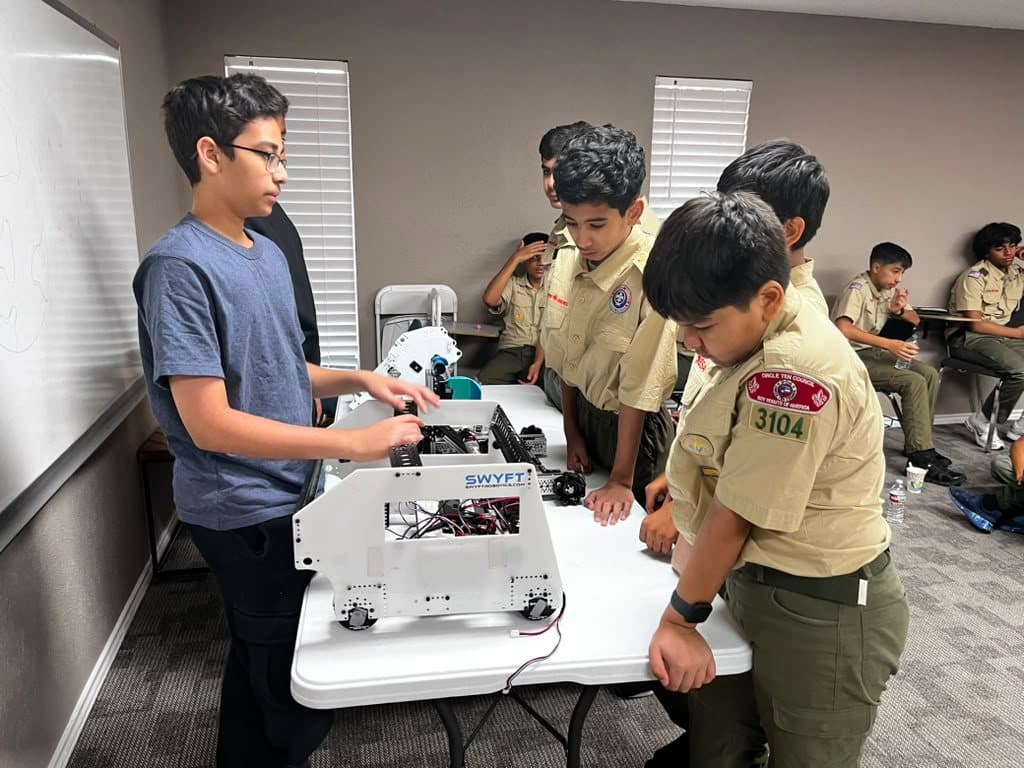 A team member shows the robot to Boy Scouts from Troop 3104 gathered around the table