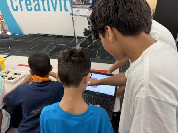 An ITKAN mentor points at a keychain design on a student's laptop screen while another student watches