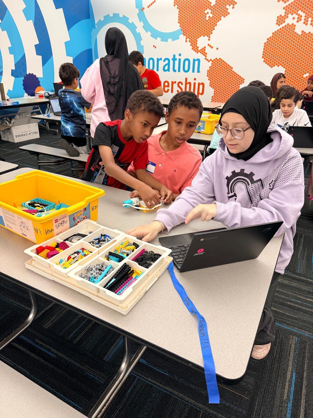 An ITKAN mentor helps two younger Ma'ruf students build with a LEGO robotics kit