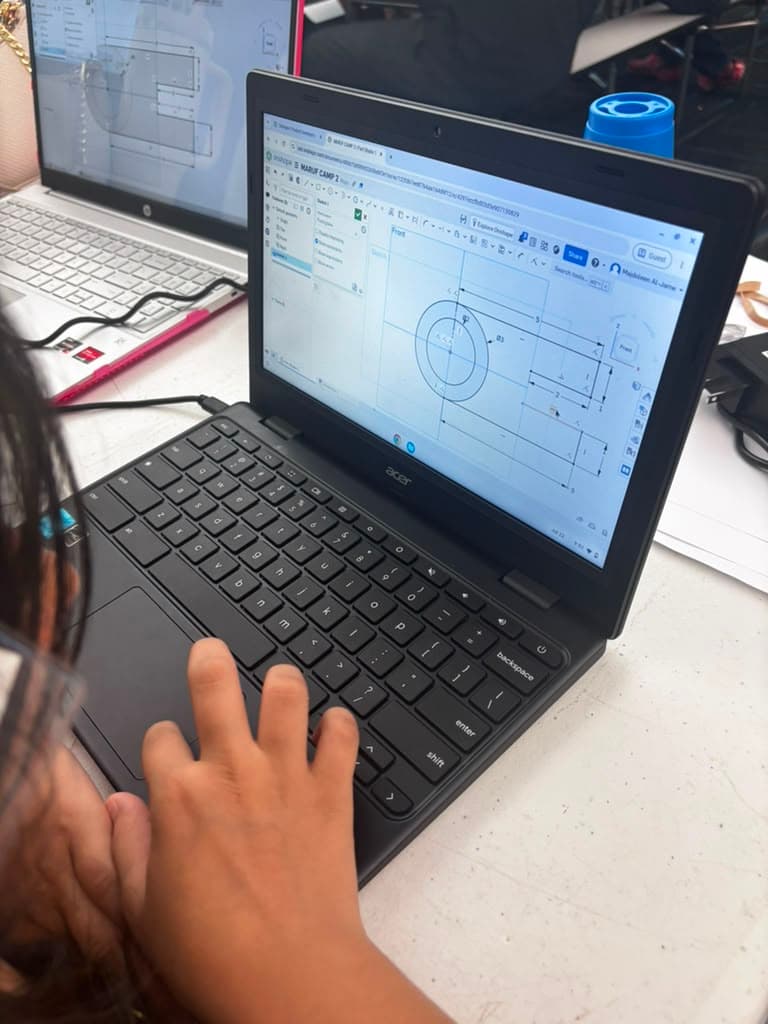 A close-up of an Onshape sketch with circular and linear dimensions on a student's laptop