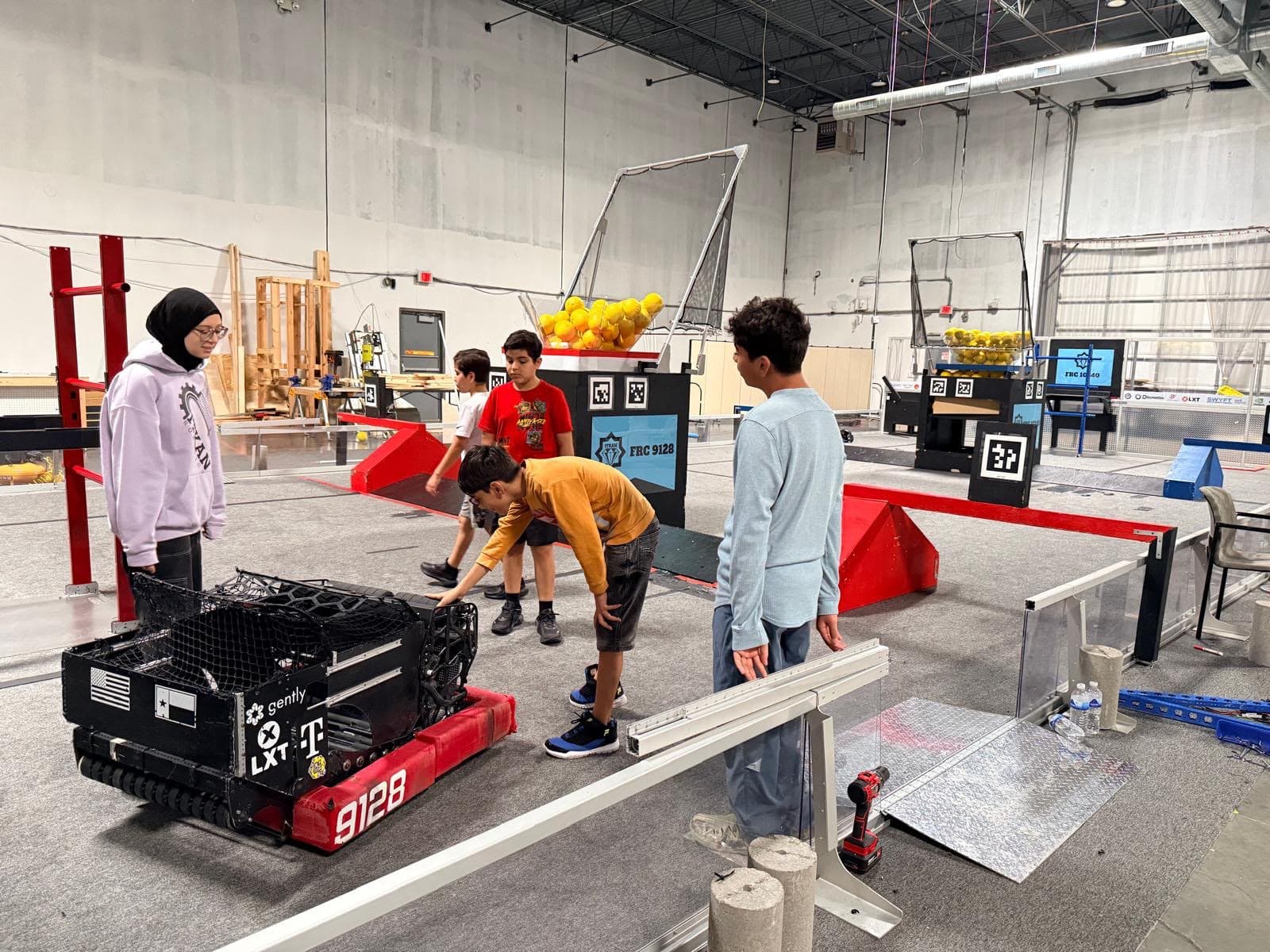 Ma'ruf students gather around ITKAN's FRC 9128 robot on the competition field at the Innovation Hub