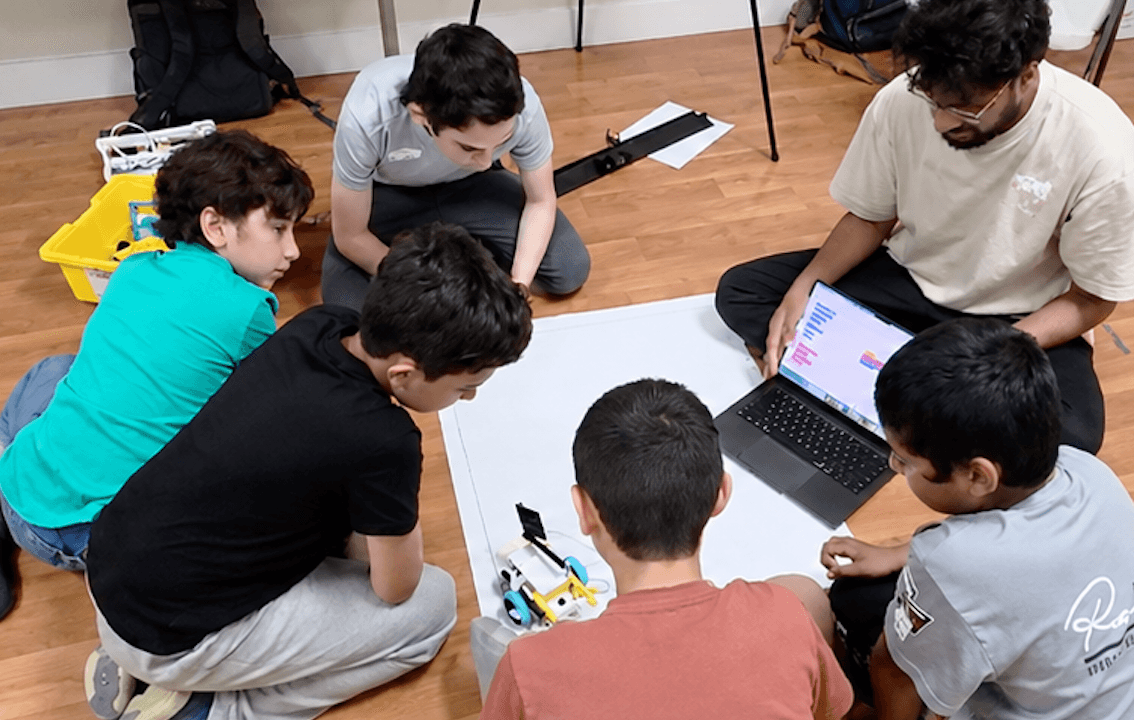 Students and a mentor gather around a laptop and robot components during ITKAN–MAS Portland's first session