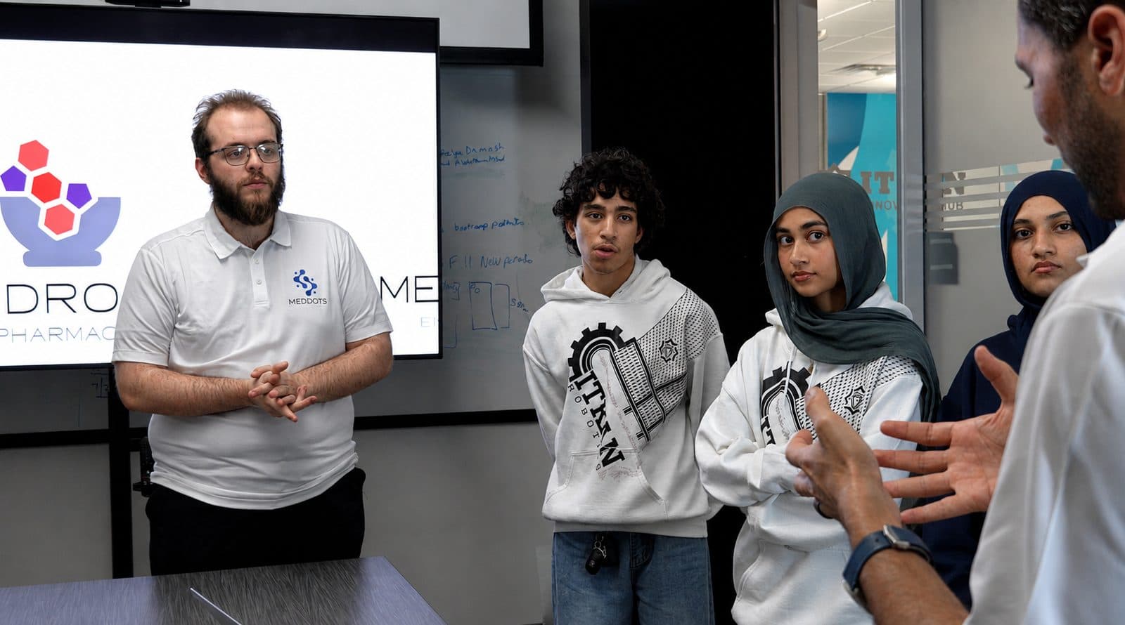 A MedDots engineer briefing three ITKAN students in front of a screen showing the Medrock and MedDots logos, with Ashraf Ahmed at the right
