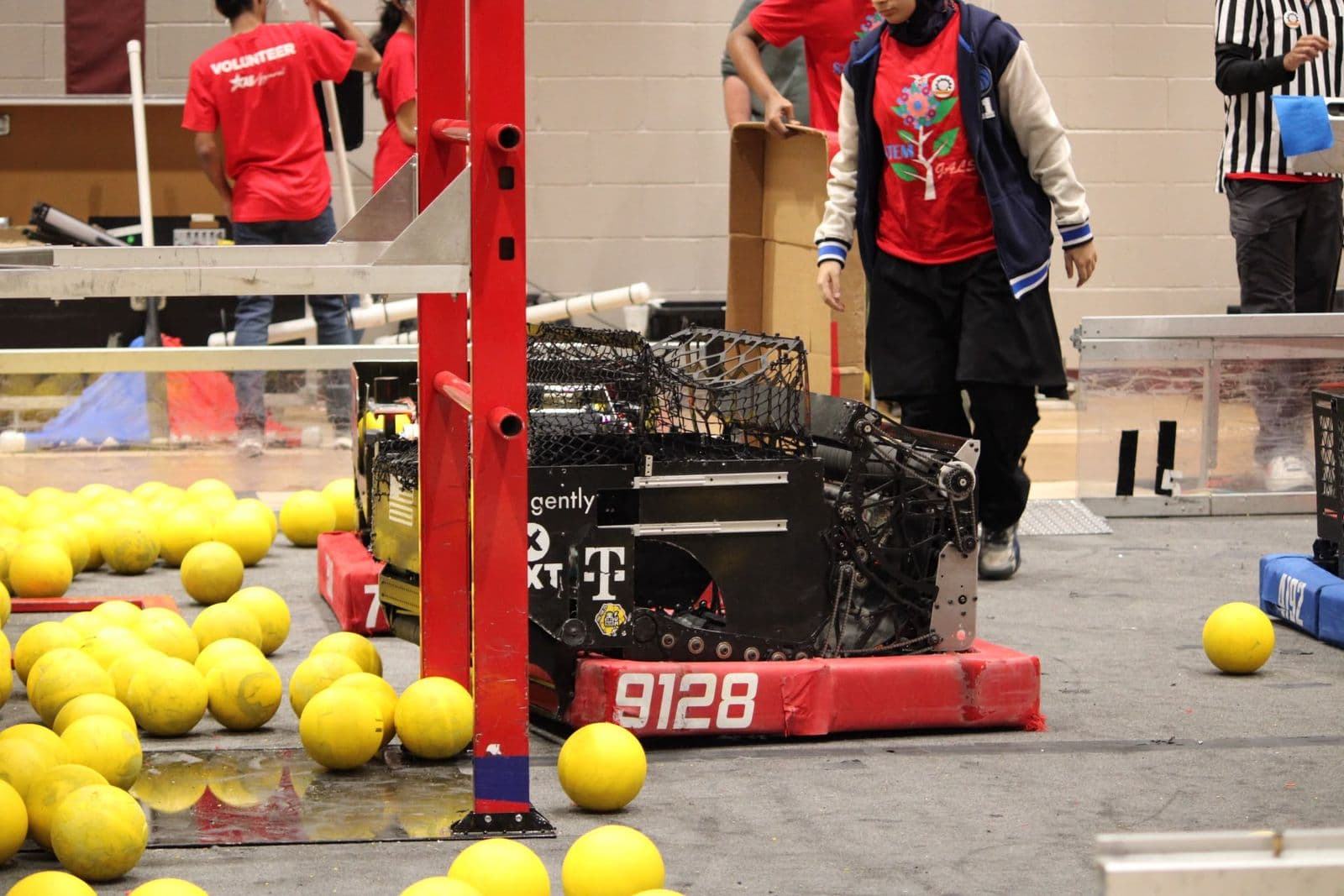 The 9128 robot in red bumpers beside a red field structure, surrounded by yellow game pieces