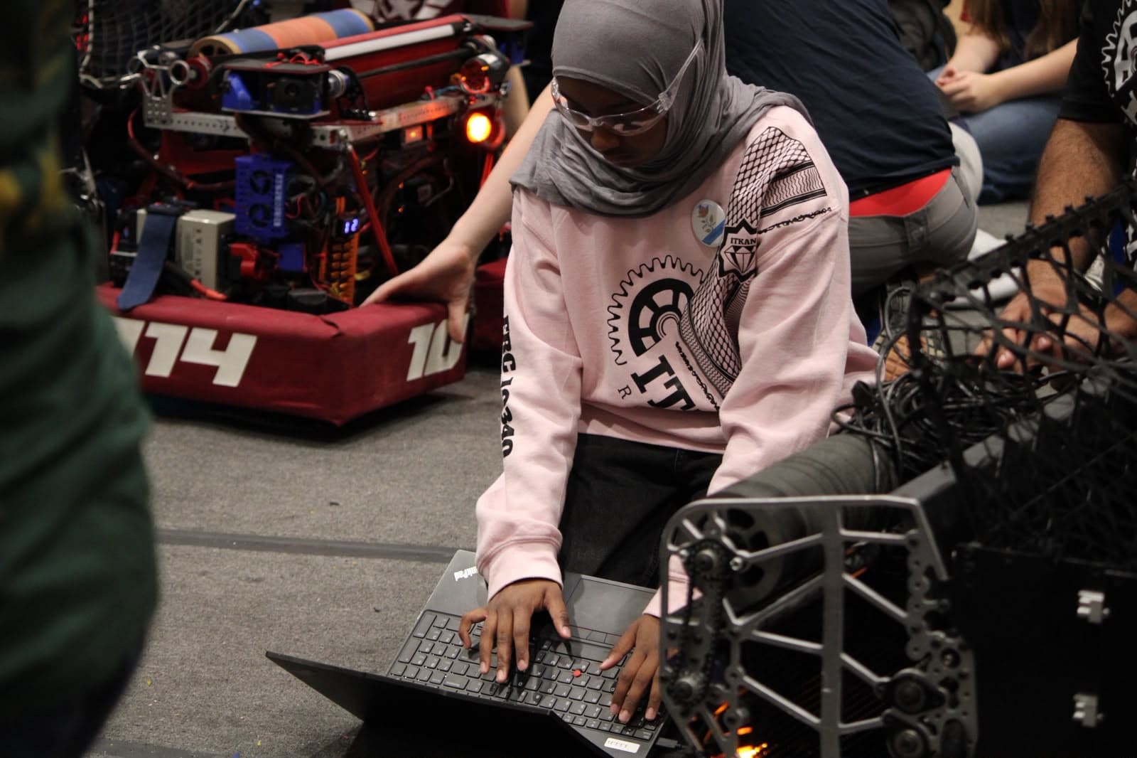 A 10340 team member in safety glasses types on a laptop beside robots on the field