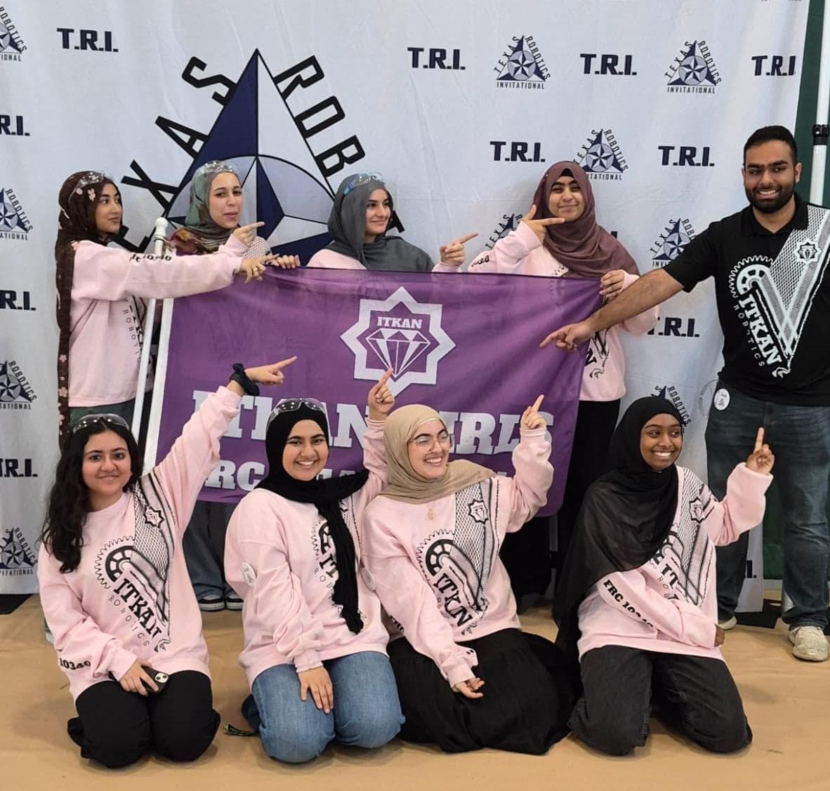 ITKAN Girls 10340 members pose with their purple ITKAN Girls FRC banner in front of the TRI backdrop